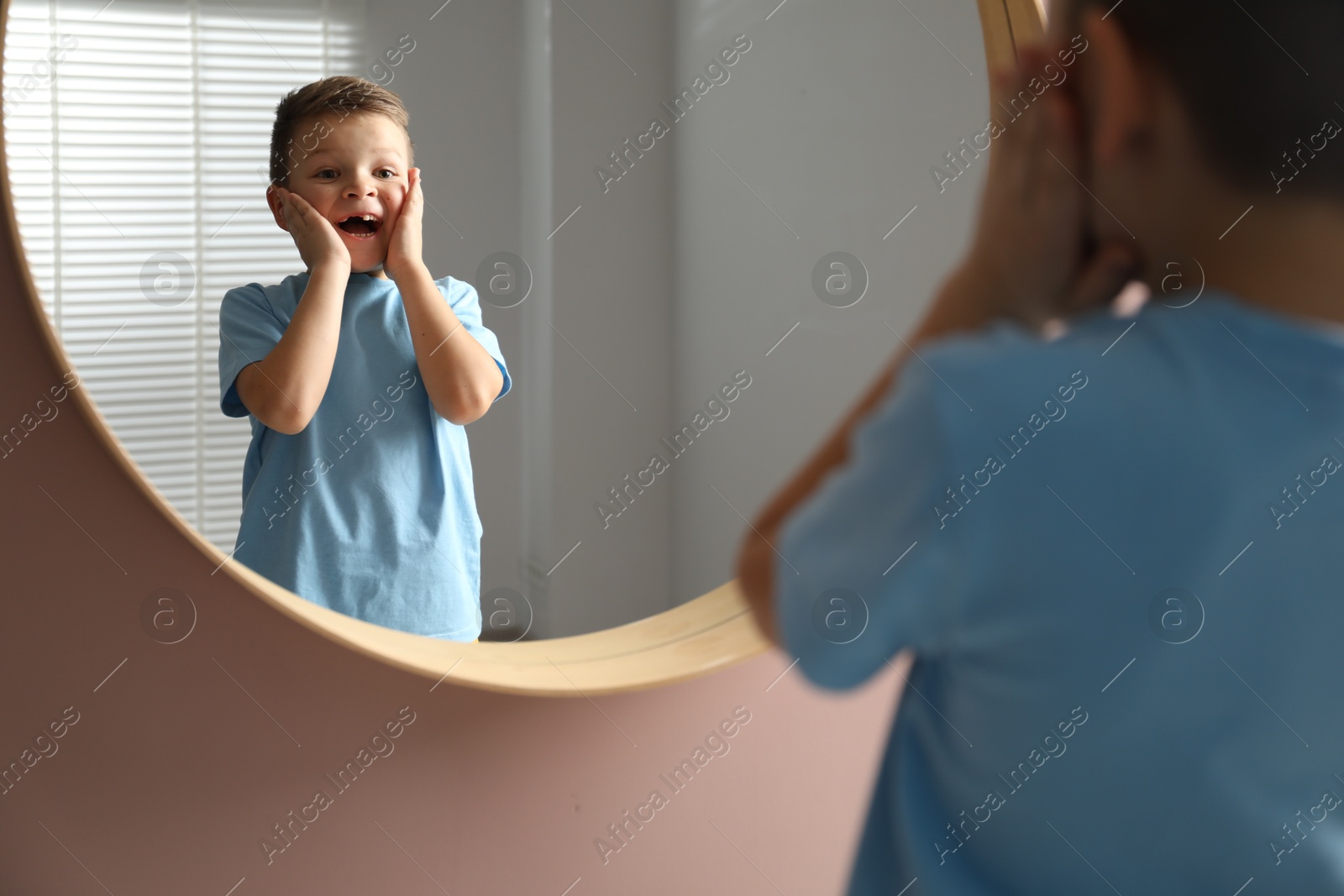 Photo of Cute little boy with missing tooth near mirror indoors