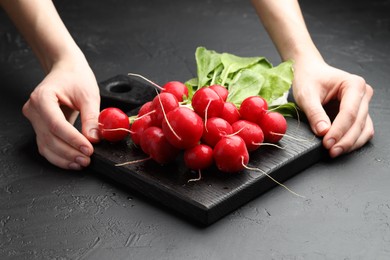 Photo of Woman with board of fresh radishes at dark textured table, closeup