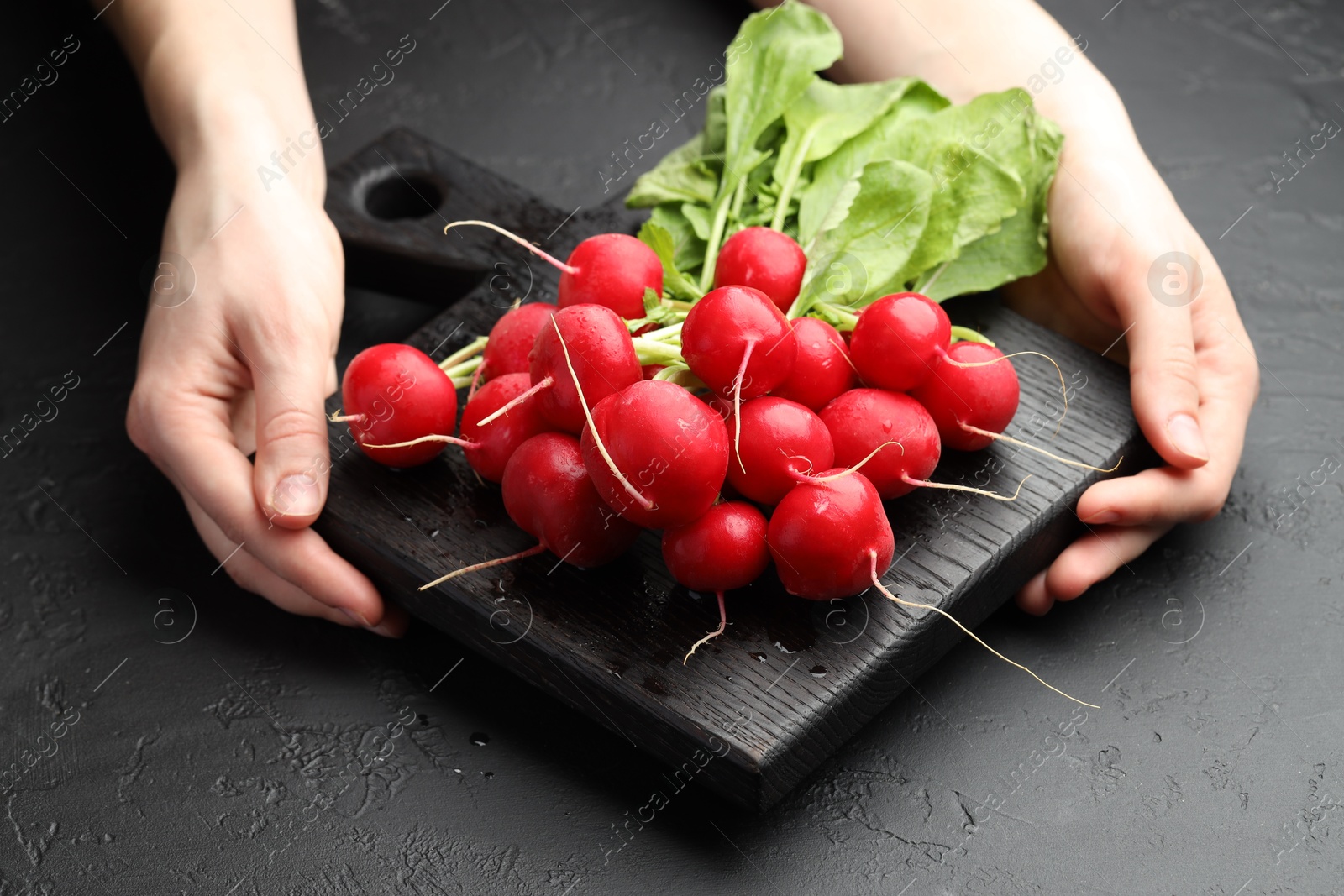 Woman with board of fresh radishes at dark textured table, closeup Photo of Woman with board of fresh radishes at dark textured table, closeup