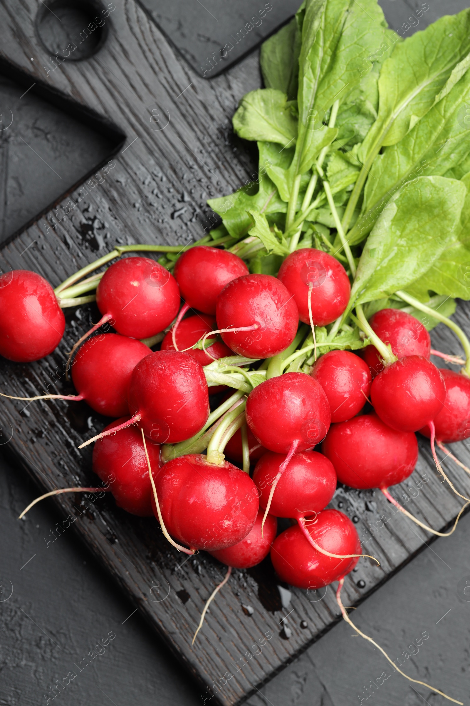 Photo of Many fresh radishes on dark textured table, top view