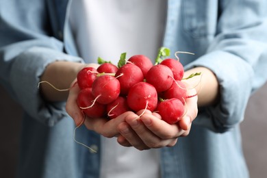 Photo of Woman with pile of fresh radishes on blurred grey background, closeup
