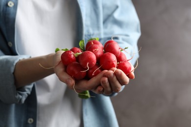 Photo of Woman with pile of fresh radishes on blurred grey background, closeup. Space for text