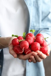 Photo of Woman with pile of fresh radishes on blurred grey background, closeup