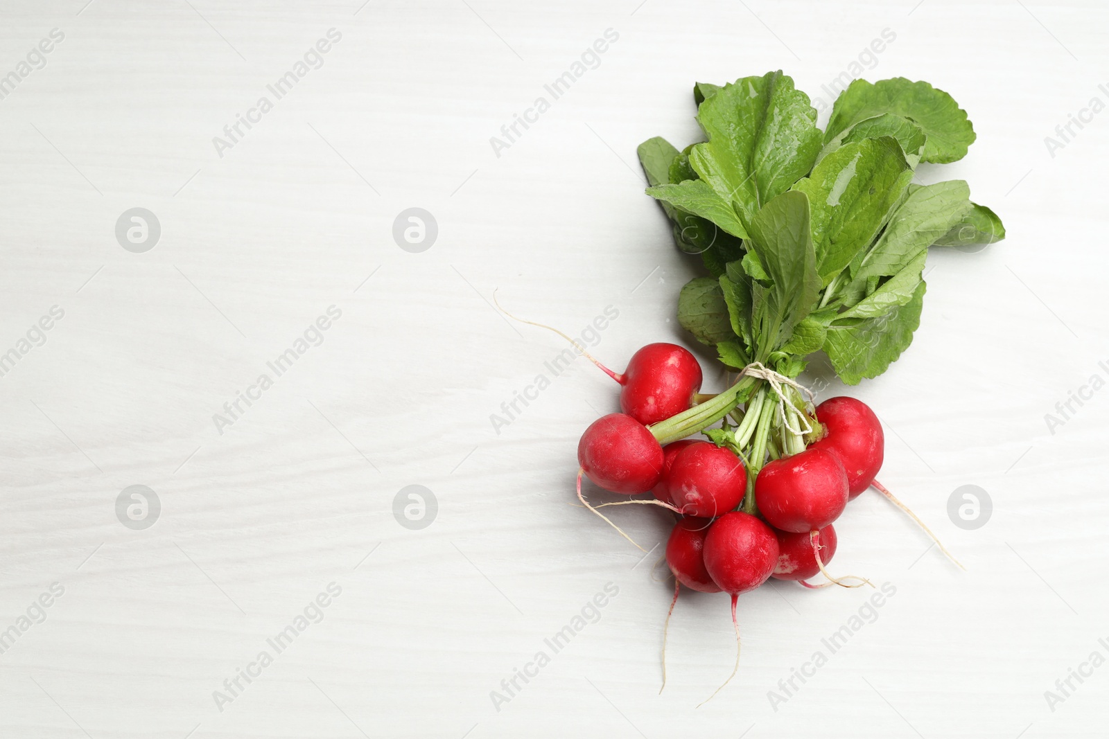 Photo of Bunch of fresh radishes on white wooden table, top view. Space for text