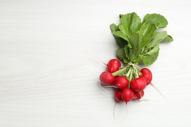 Photo of Bunch of fresh radishes on white wooden table, top view. Space for text