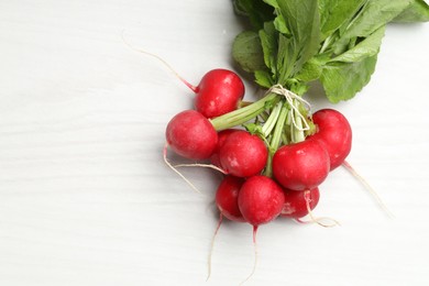 Photo of Bunch of fresh radishes on white wooden table, top view. Space for text