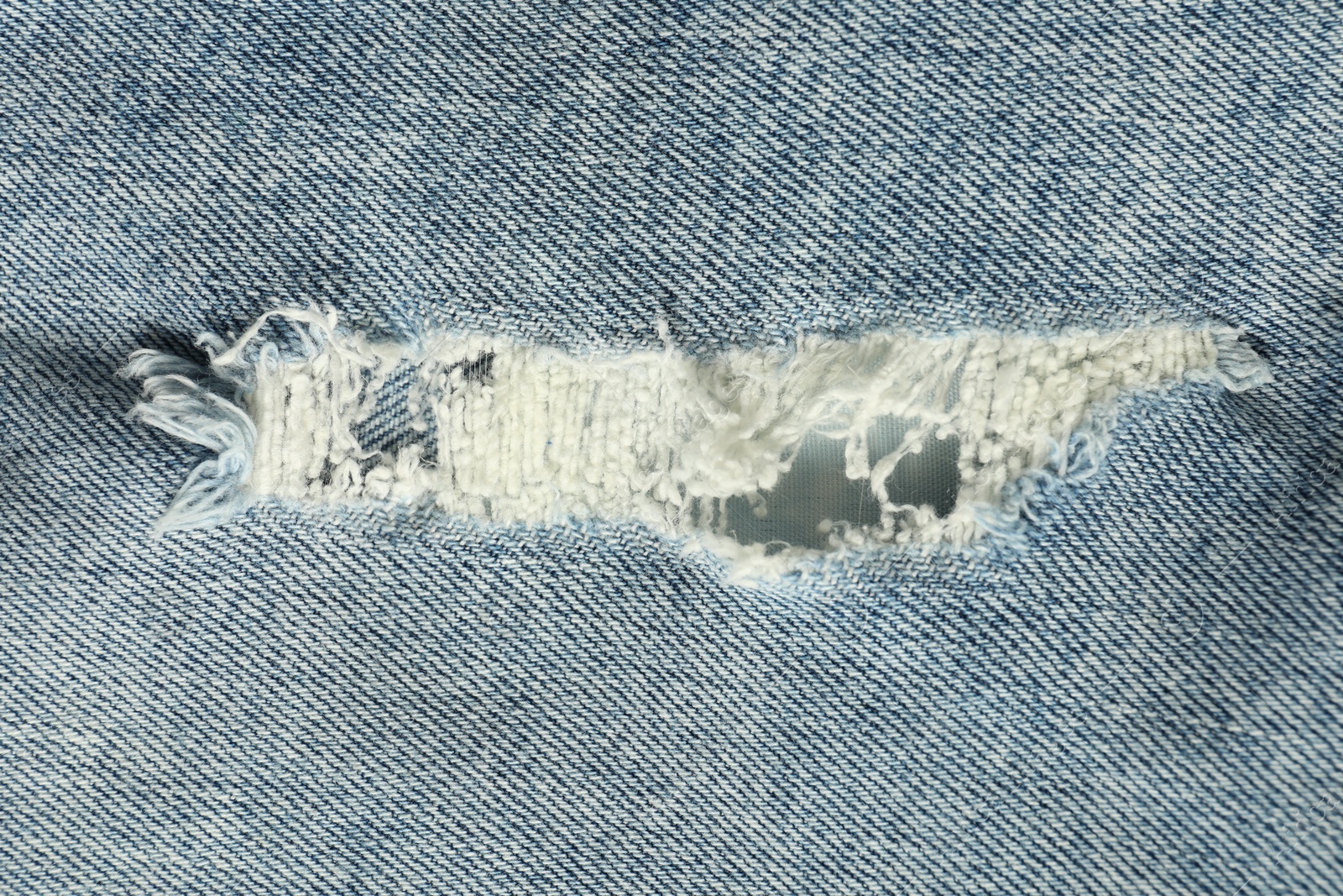 Photo of Texture of ripped light blue jeans as background, top view