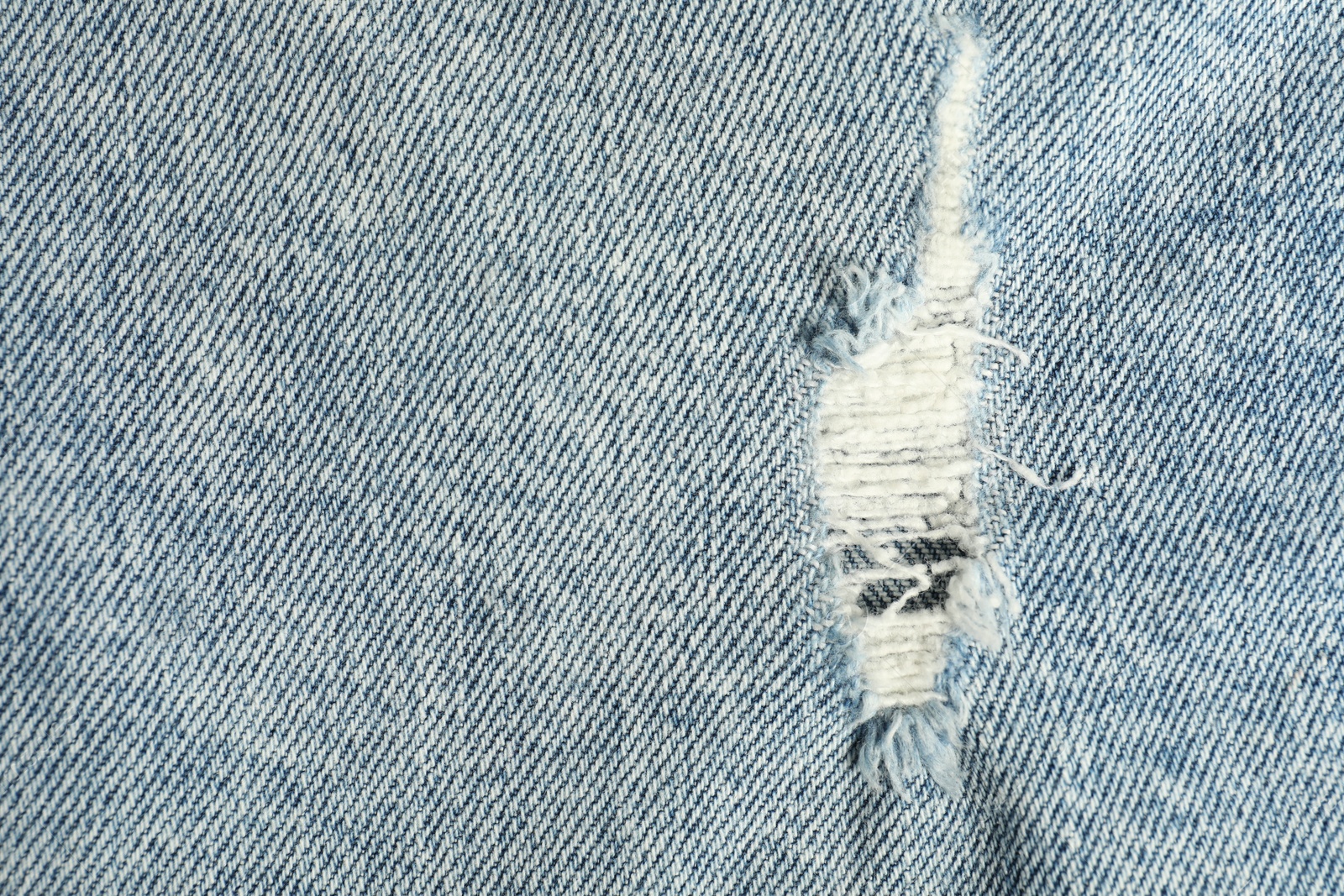 Photo of Texture of ripped light blue jeans as background, top view