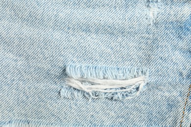 Photo of Texture of ripped light blue jeans as background, top view