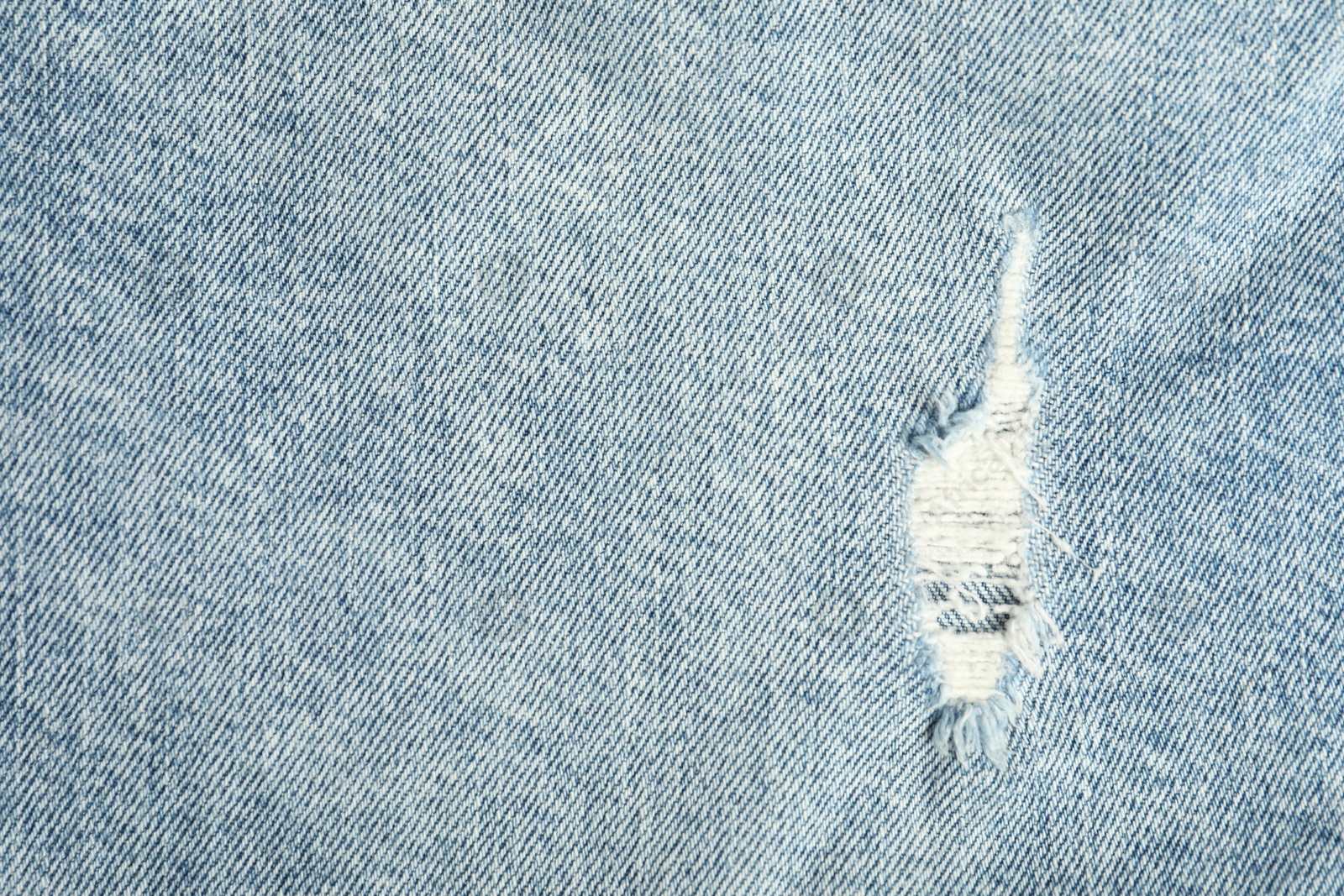 Photo of Texture of ripped light blue jeans as background, top view