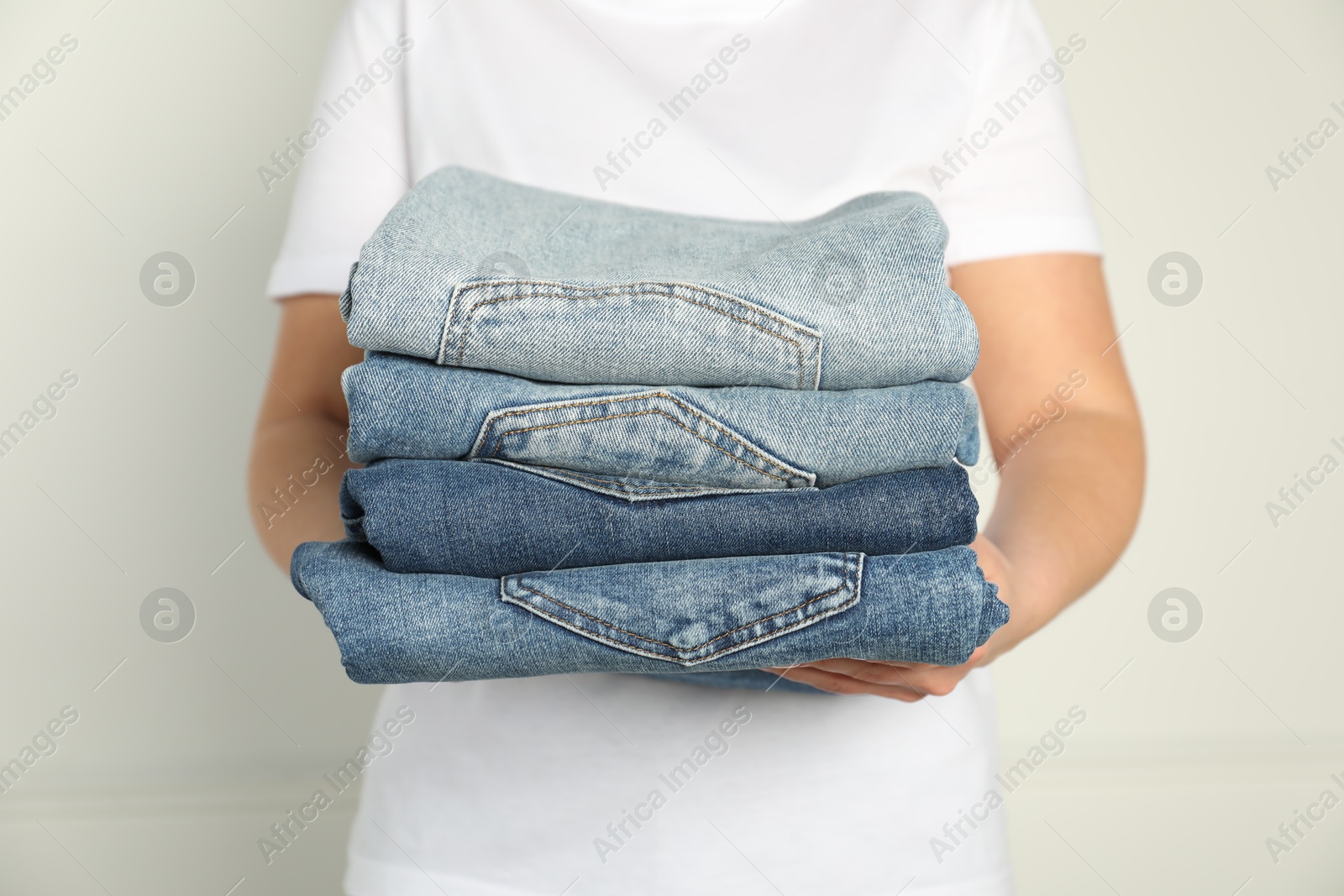 Photo of Woman with stack of different stylish jeans near light wall indoors, closeup