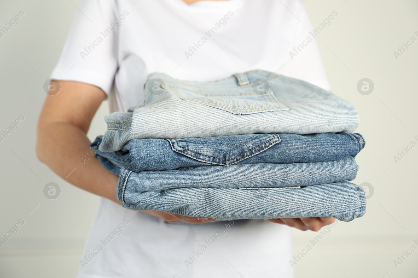 Photo of Woman with stack of different stylish jeans near light wall indoors, closeup