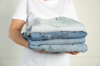 Photo of Woman with stack of different stylish jeans near light wall indoors, closeup