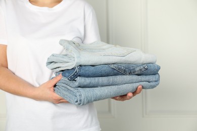 Photo of Woman with stack of different stylish jeans near light wall indoors, closeup