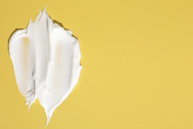 Photo of Cream on yellow background, top view. Sample of cosmetic product. Space for text