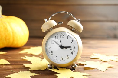 Photo of Autumn time. Alarm clock and golden leaves on wooden table