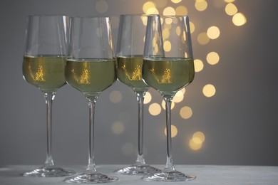 Tasty white wine in glasses on table against grey background with blurred lights, bokeh effect. Space for text