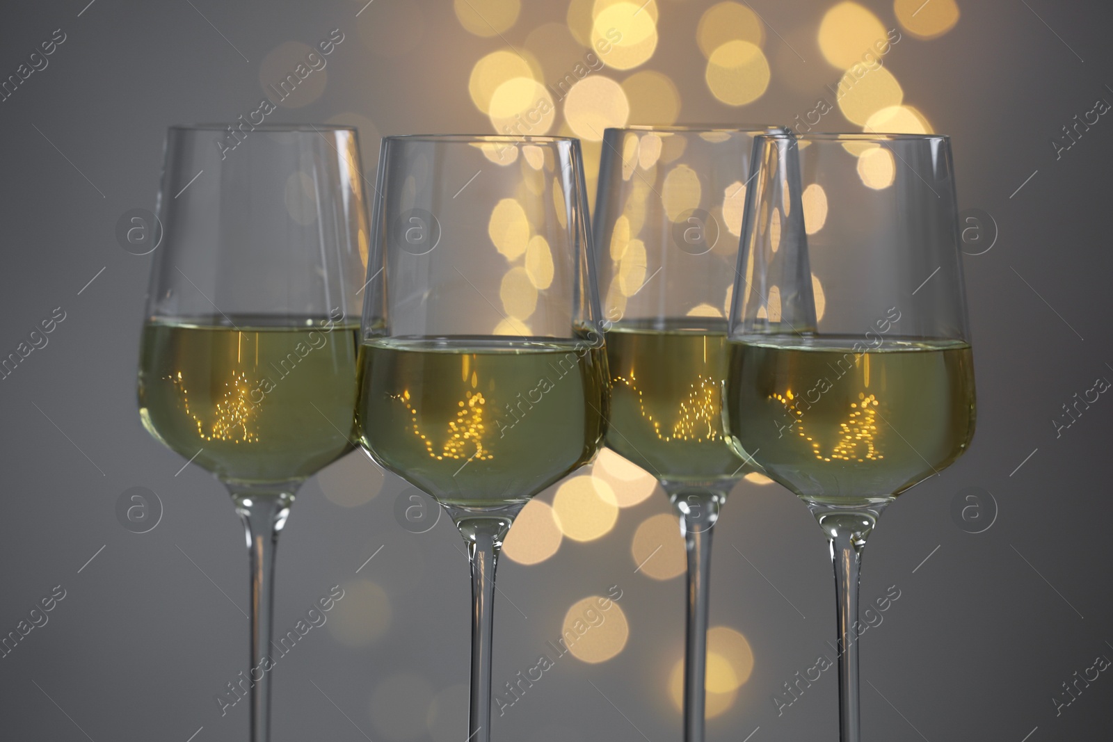 Photo of Tasty white wine in glasses against grey background with blurred lights, closeup. Bokeh effect