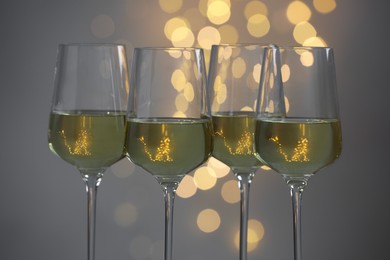 Tasty white wine in glasses against grey background with blurred lights, closeup. Bokeh effect