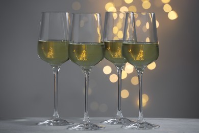 Tasty white wine in glasses on table against grey background with blurred lights, bokeh effect