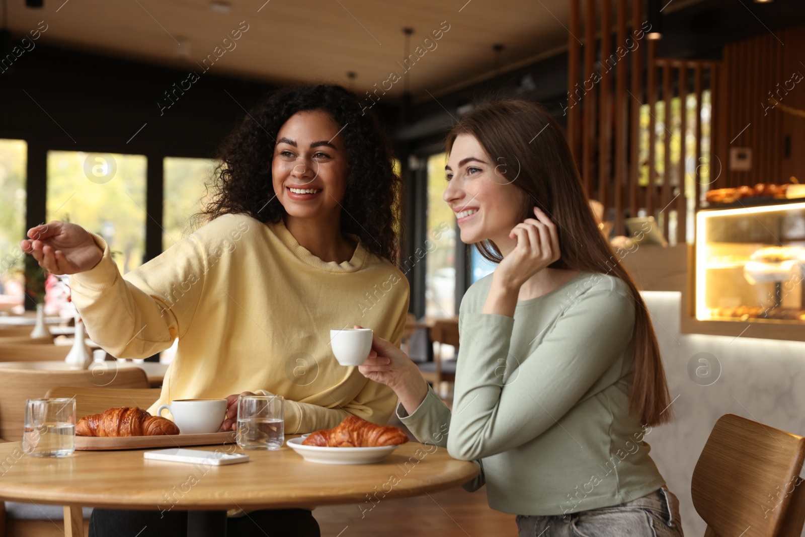 Photo of Happy women with coffee drinks chatting in cafe