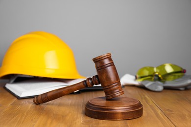 Photo of Accident at work concept. Gavel, book and construction worker's protective gear on wooden table, selective focus