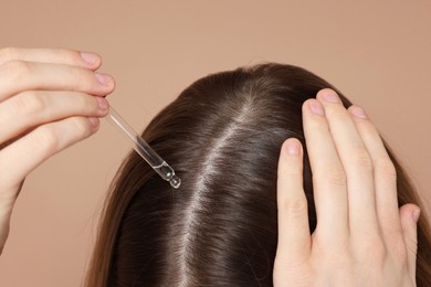 Photo of Hair loss problem. Girl applying serum onto hairline on dark beige background, closeup