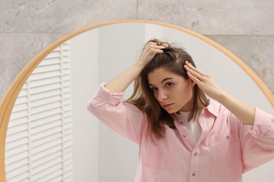 Photo of Girl with hair loss problem near mirror in bathroom