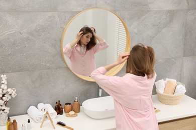 Photo of Girl with hair loss problem near mirror in bathroom