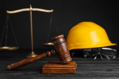 Photo of Accident at work concept. Gavel, scales and construction worker's protective gear on black wooden table, selective focus