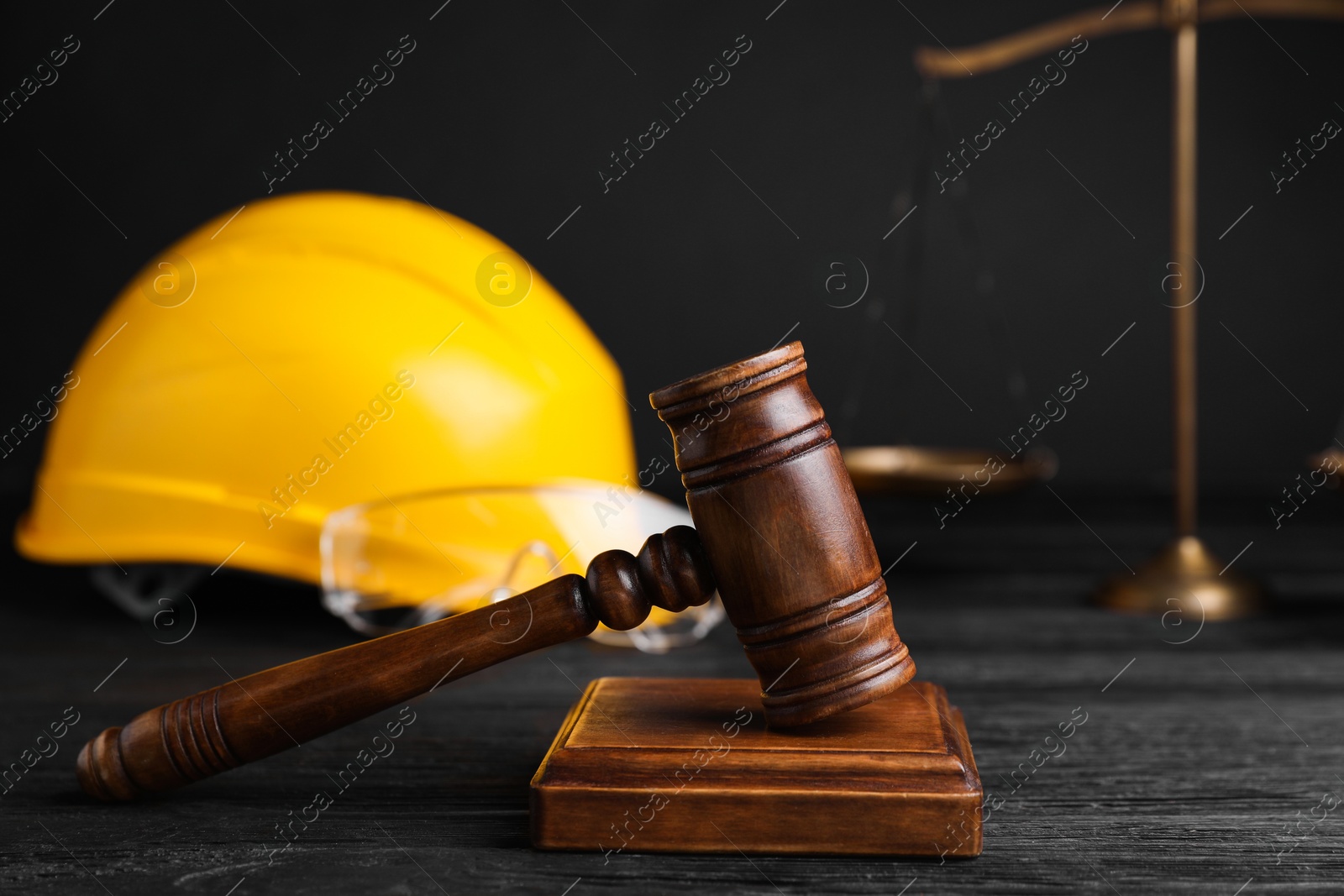 Photo of Accident at work concept. Gavel, scales and construction worker's protective gear on black wooden table, selective focus