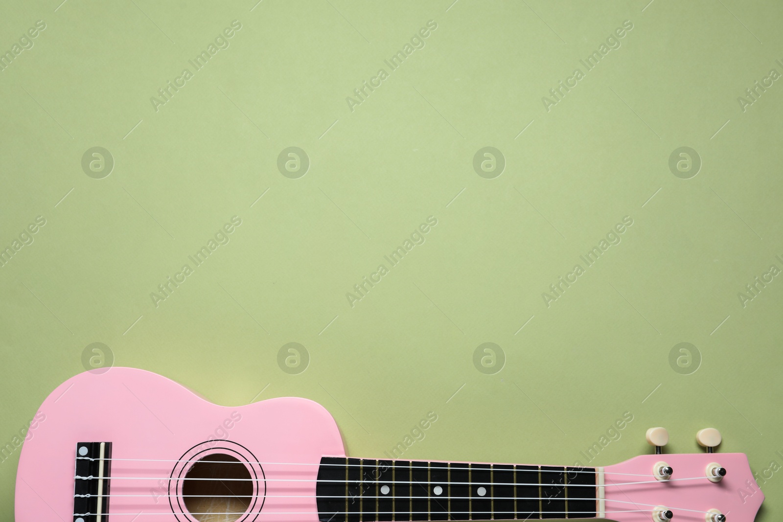 Photo of One ukulele on light olive background, top view. Space for text