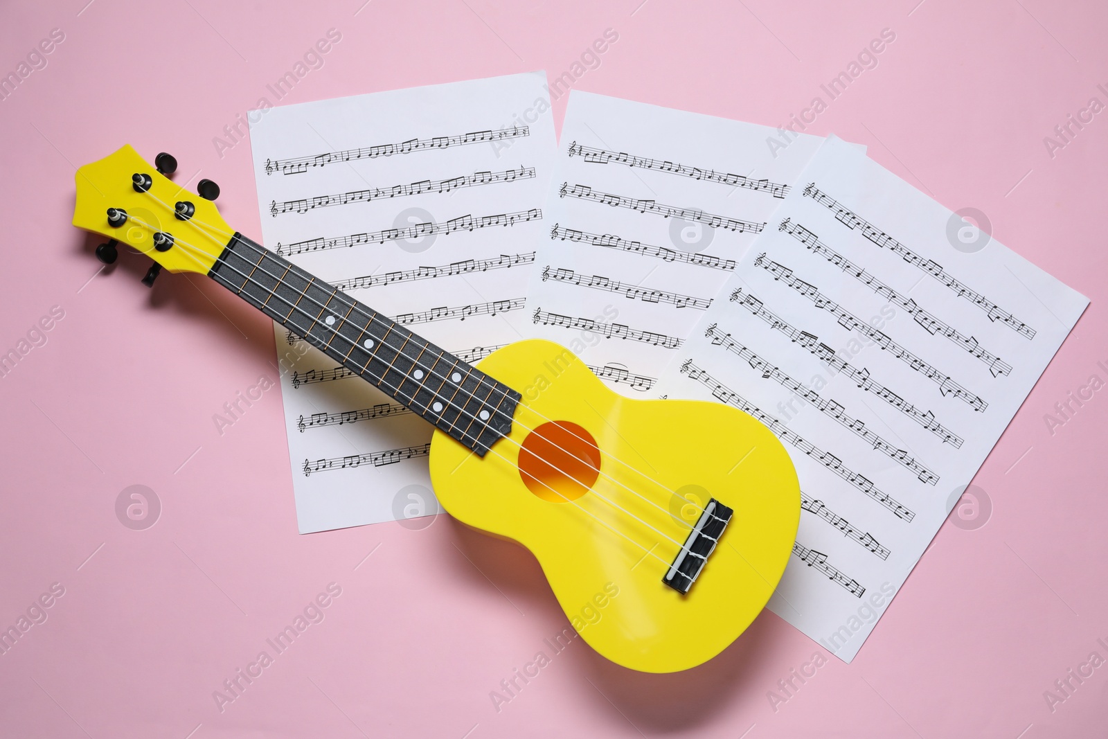 Photo of Ukulele and music sheets on pink background, top view