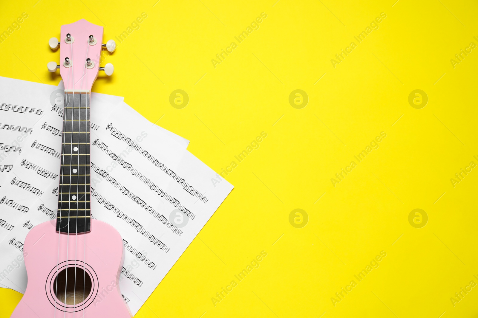 Photo of Ukulele and music sheets on yellow background, top view. Space for text