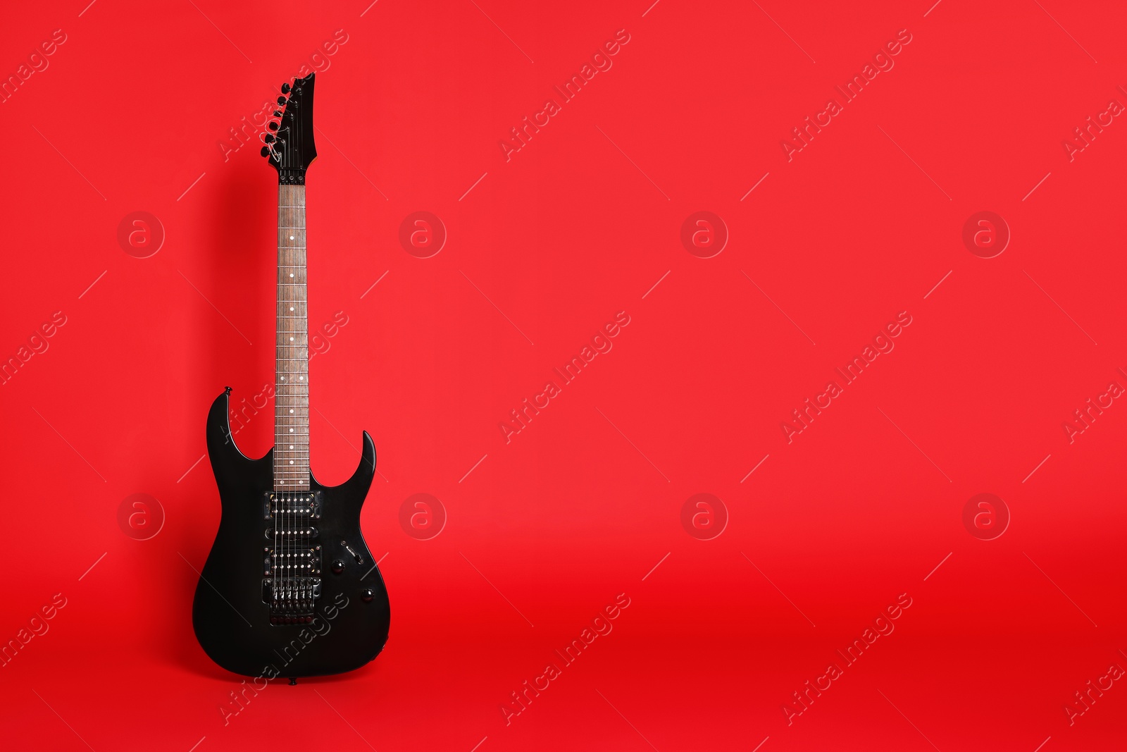 Photo of One modern electric guitar on red background. Space for text