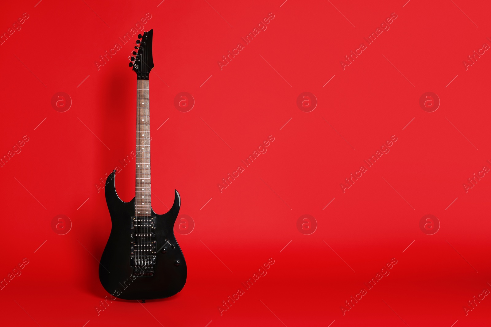 Photo of One modern electric guitar on red background. Space for text