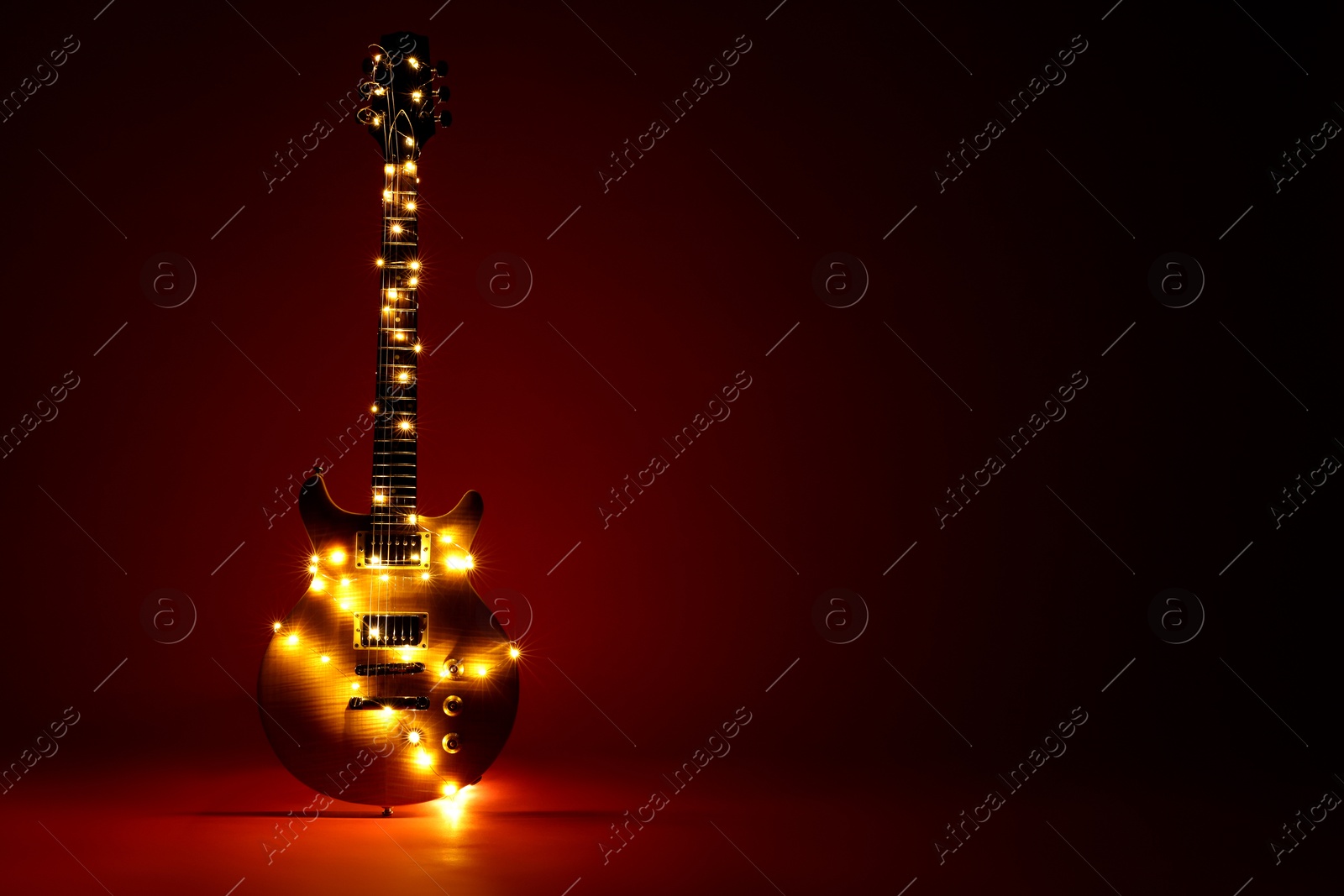 Photo of Electric guitar with Christmas lights on dark red background. Space for text