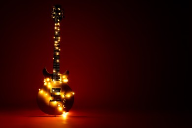 Photo of Electric guitar with Christmas lights on dark red background. Space for text