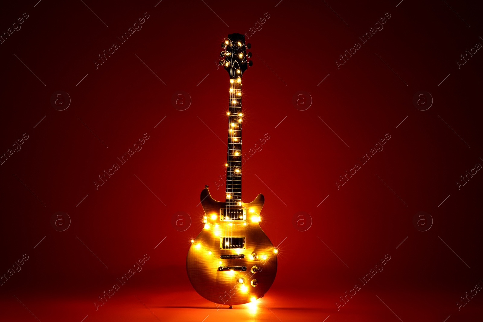 Electric guitar with Christmas lights on dark red background Photo of Electric guitar with Christmas lights on dark red background