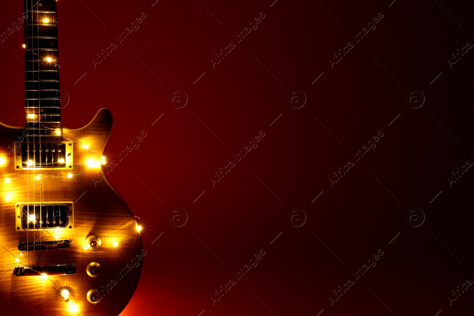 Photo of Electric guitar with Christmas lights on dark red background, closeup. Space for text