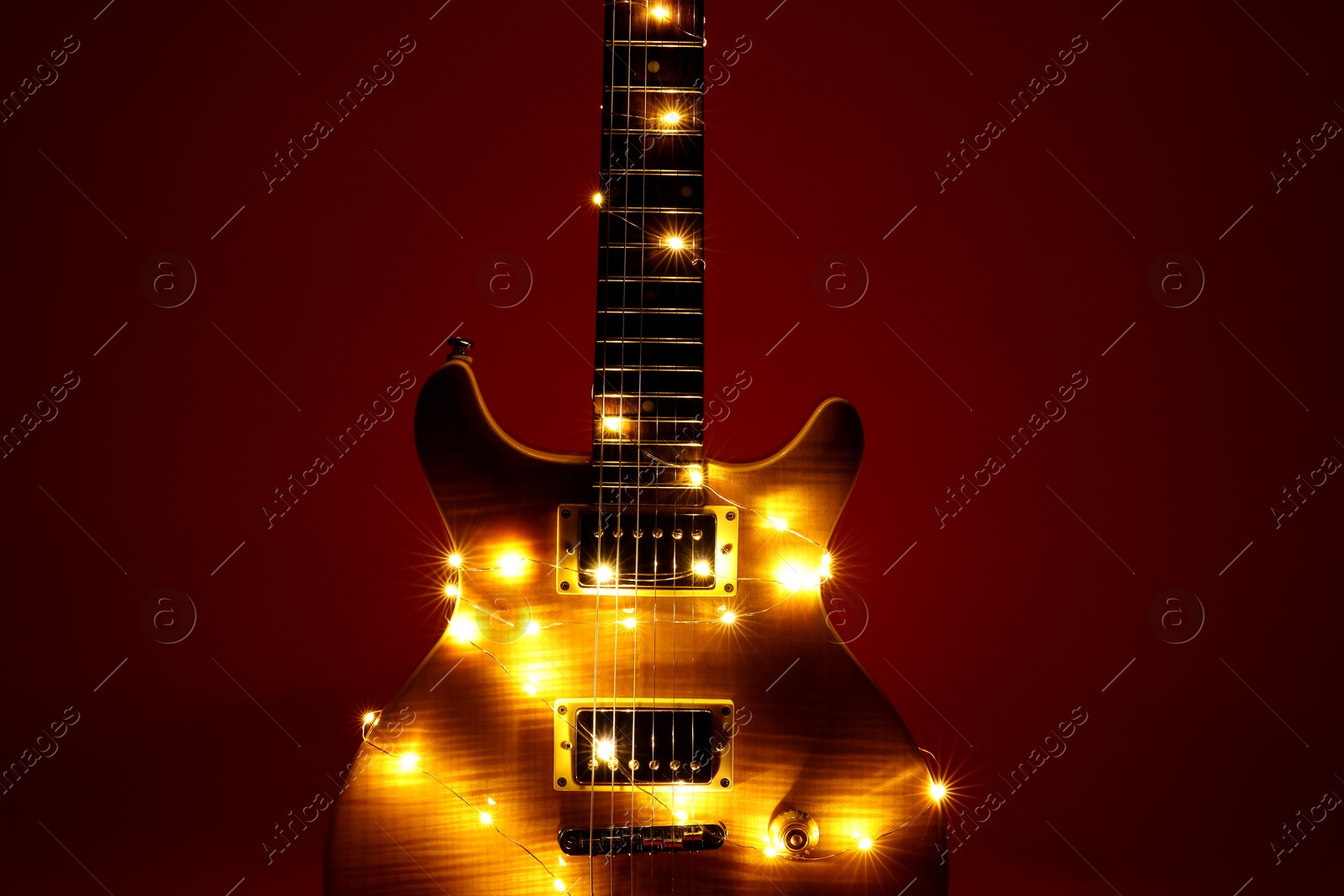 Photo of Electric guitar with Christmas lights on dark red background, closeup