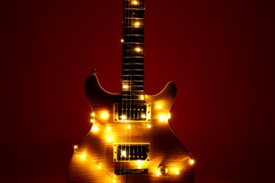 Photo of Electric guitar with Christmas lights on dark red background, closeup