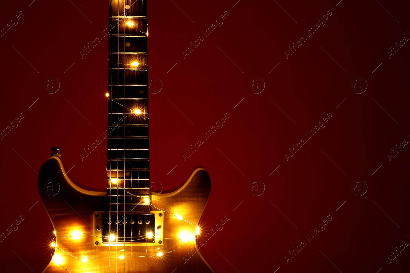 Photo of Electric guitar with Christmas lights on dark red background, closeup. Space for text