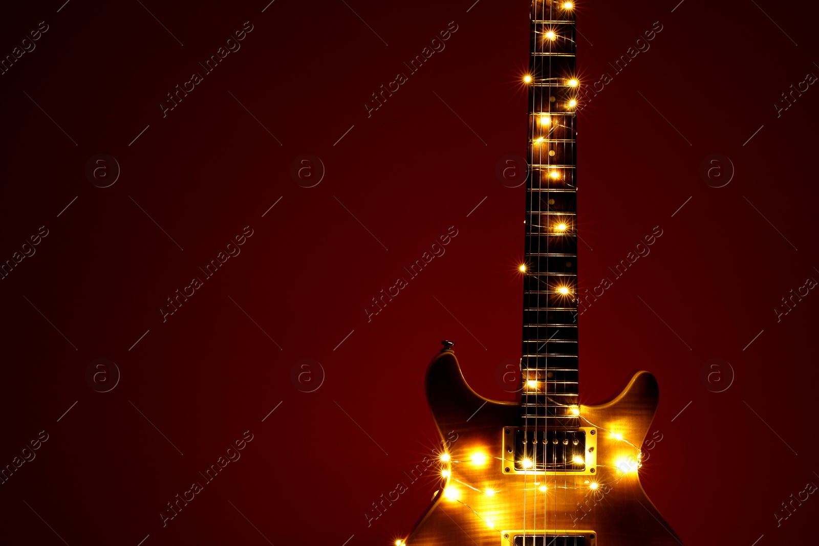 Photo of Electric guitar with Christmas lights on dark red background. Space for text