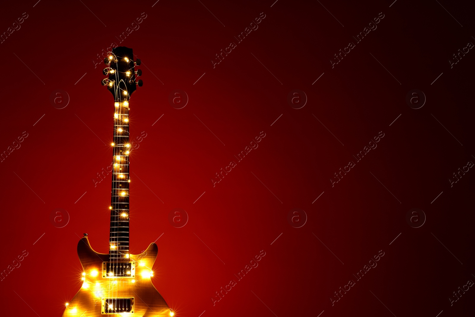 Photo of Electric guitar with Christmas lights on dark red background. Space for text