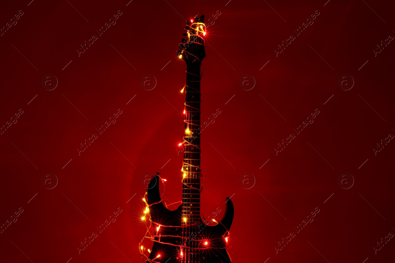 Photo of Electric guitar with Christmas lights on dark red background