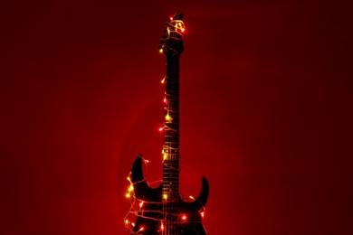 Electric guitar with Christmas lights on dark red background