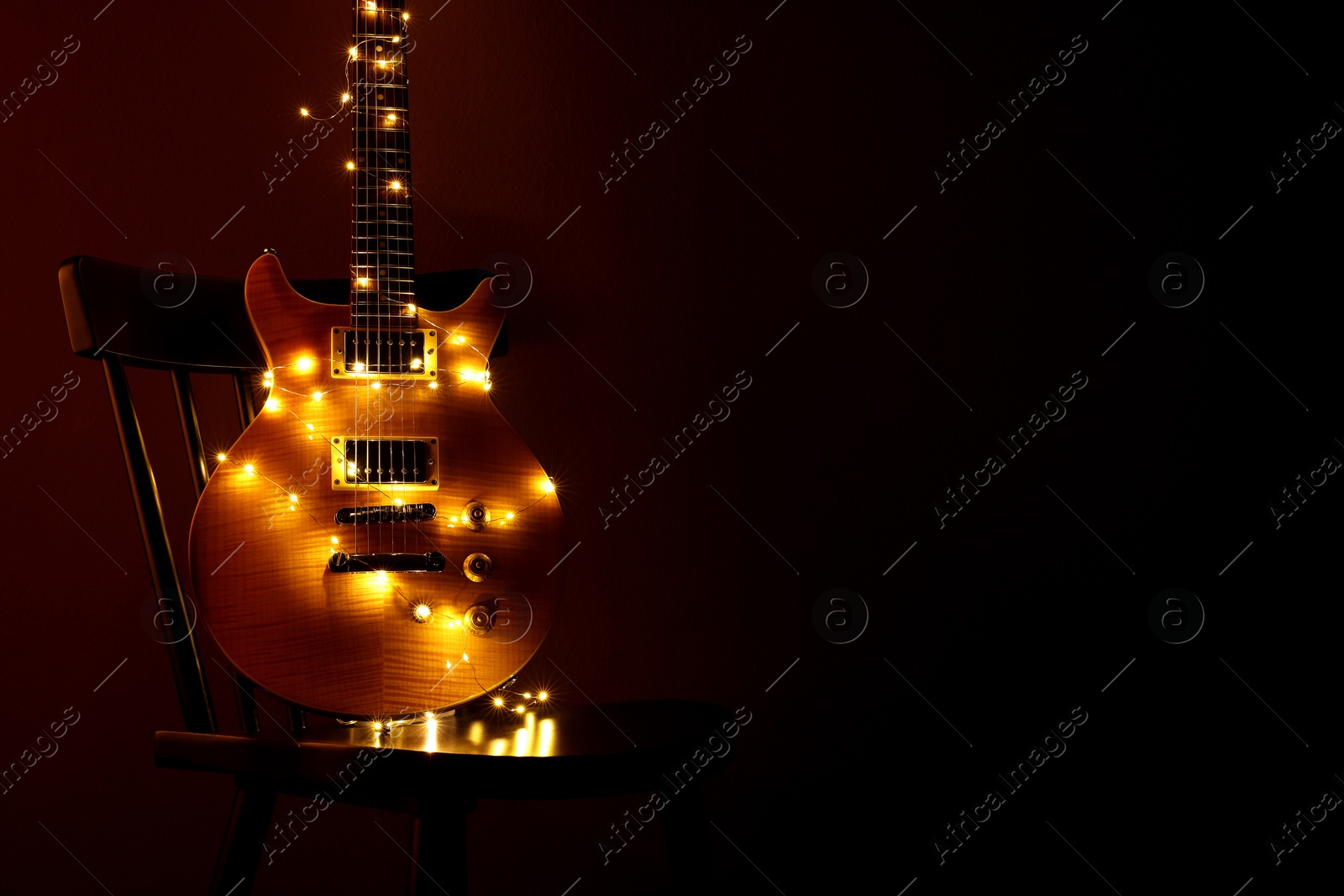 Photo of Electric guitar with Christmas lights on chair against dark background. Space for text