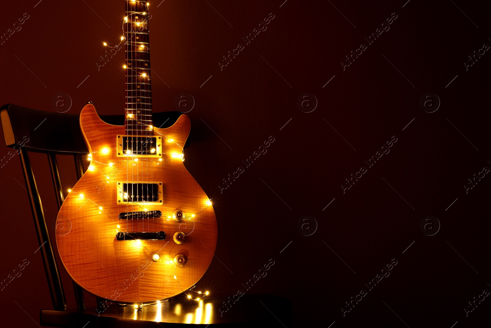 Photo of Electric guitar with Christmas lights on chair against dark background. Space for text