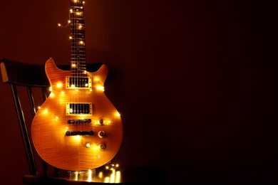 Photo of Electric guitar with Christmas lights on chair against dark background. Space for text